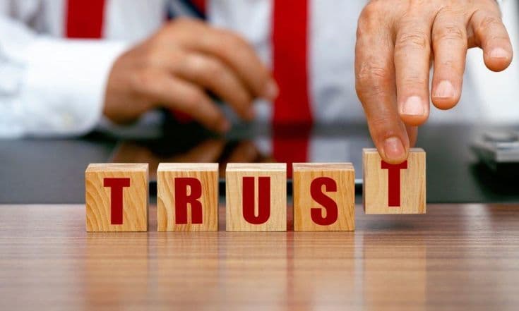 A hand steadying wooden blocks that spell TRUST
