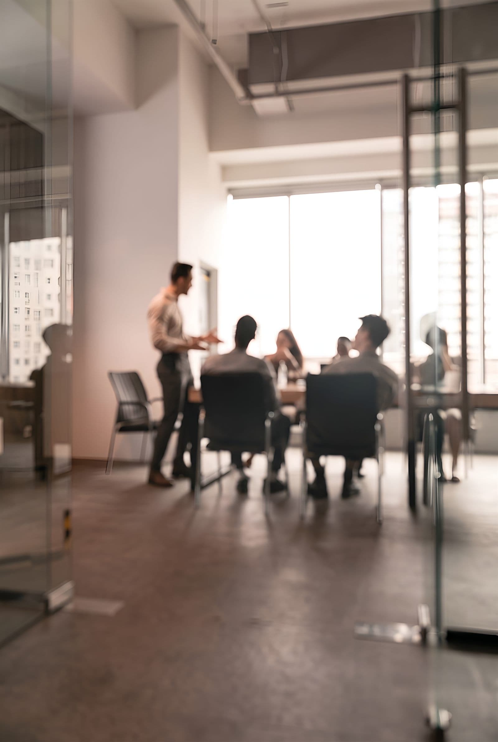 A leader presenting to a seated leadership team in a glass-walled office