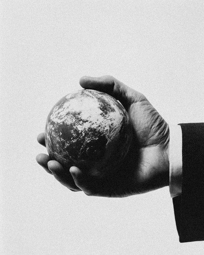 A suited arm holding a small globe in an open palm