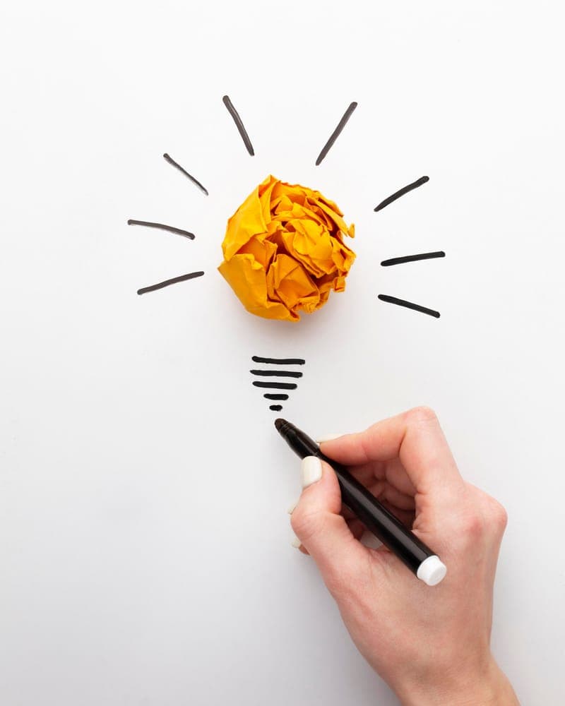 A hand drawing lightbulb rays around a crumpled ball of orange paper